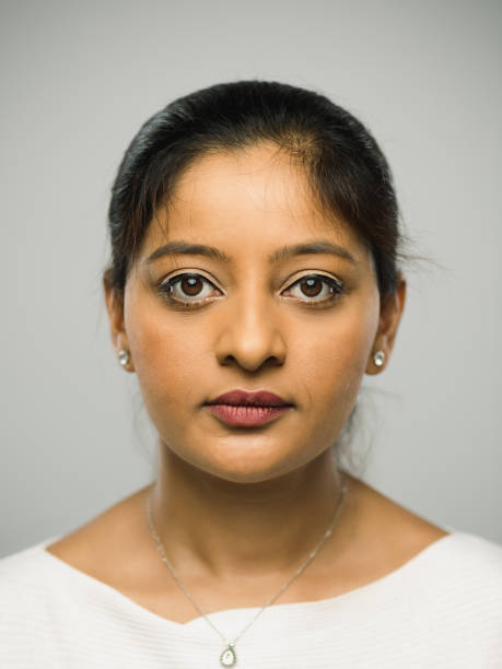 Close up portrait of indian young woman with blank expression against gray background. Vertical shot of real woman staring in studio with long black hair. Photography from a DSLR camera. Sharp focus on eyes.